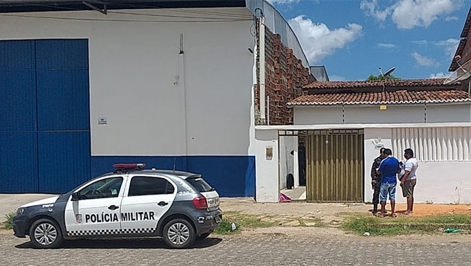   Imagem mostra PM conversando com os blogueiros Nilson Ferreira e Junior, em frente a casa que aconteceu o assassinato no bairro Ouro Negro (Aeroporto), em Mossoró; corpo da vítima está coberto com um pano vermelho perto do portão