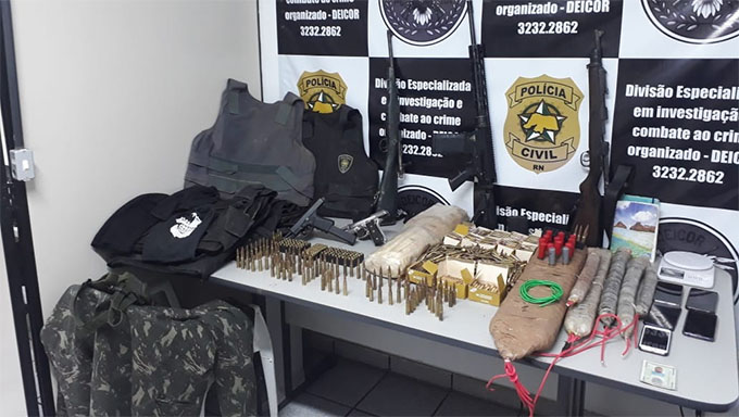 Imagem 1 -  Com o criminoso Camilo Bombado, foi apreendido: 03 fuzis de calibres 5,56 e 7,62, aproximadamente mil munições calibre 5,56, 90 munições de calibre 7,62, 13 munições de calibre 12, 142 munições de calibre 9mm, mais de 20kg de explosivos, 6 coletes balísticos (sendo um da PMRN e outro da PCRN), balaclava e roupas utilizadas nas ações criminosas. Veja vídeo do local que Camilo Bombado escondia as armas.