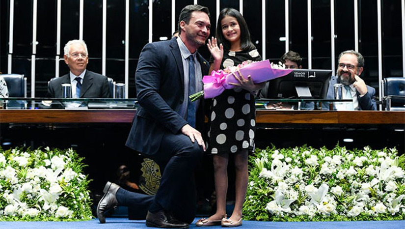 Imagem 1 - Durante a sessão, a vida de Tiffany Brito, de 8 anos, foi celebrada. Ela recebeu flores das mãos do senador Styvenson Valentim (Podemos-RN) e retribuiu o presente com um desenho em que a menina aparece ao lado do senador. "Quero te homenagear em nome de todas as crianças que estão lutando contra o câncer", disse o senador Styvenson Valentin, que propôs e presidiu a sessão no Senado Federal em homenagem as vítimas do câncer. Na ocasião, defendeu o tratamento precoce. Imagem 1 - Durante a sessão, a vida de Tiffany Brito, de 8 anos, foi celebrada. Ela recebeu flores das mãos do senador Styvenson Valentim (Podemos-RN) e retribuiu o presente com um desenho em que a menina aparece ao lado do senador. "Quero te homenagear em nome de todas as crianças que estão lutando contra o câncer", disse o senador Styvenson Valentin, que propôs e presidiu a sessão no Senado Federal em homenagem as vítimas do câncer. Na ocasião, defendeu o tratamento precoce.