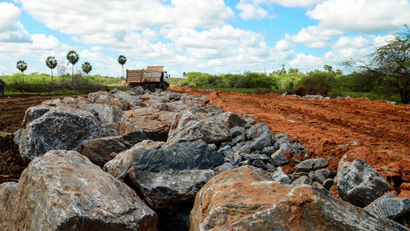 Imagem 1 -  A obra está atualmente na fase de troca de solo, que acontece de forma planejada, de acordo com estudos técnicos. Inicialmente é realizada a limpeza de toda a extensão da área, em seguida acontece a retirada do solo mole para colocação da pedra rachão, utilizada como base de pavimentação, terraplenagem e drenagem. Essa fase das obras é essencial para atender à necessidade de compactação do terreno garantindo que a via seja entregue conforme planejada. Que passará a contar com uma circulação mais fluida de veículos na região. A obra representa um marco histórico para a mobilidade urbana da cidade, que irá interligar as BRs 110 e 304.