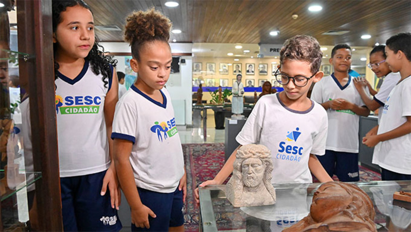 Imagem 1 -  Acompanhadas pelo professor de educação física Wenício e pela assistente social e responsável técnica do projeto, Samara Almeida, as crianças, com idades entre 8 e 15 anos, visitaram a exposição “Além do Imaginário: A arte popular potiguar, antes e depois de Xico Santeiro”, com o objetivo de ampliar seus conhecimentos de mundo e estimular um pensamento crítico e reflexivo. Atualmente, o projeto Sesc Cidadão atende 42 crianças em situação de vulnerabilidade social, proporcionando-lhes oportunidades educativas e culturais.  A mostra está aberta na na Assembleia Legislativa desde o dia 10, oferece uma imersão na rica tradição da arte popular potiguar.