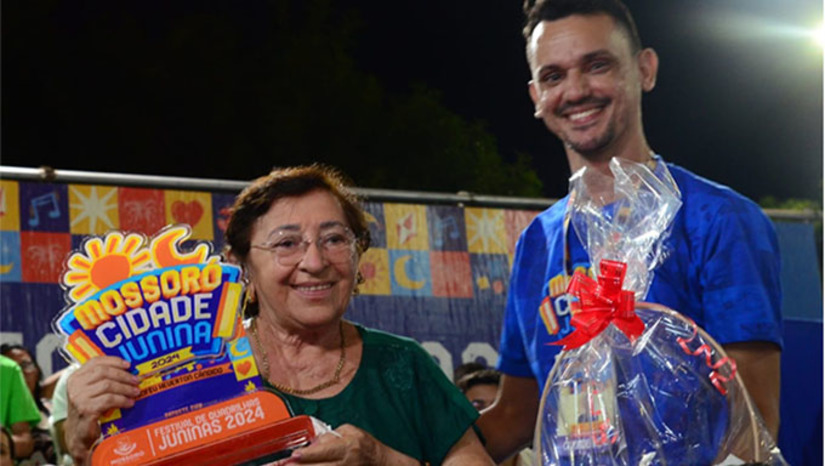 Imagem 1 -  A organização do concurso realizou homenagem e entregou um troféu à professora Deodete Dias, por sua contribuição há mais de 40 anos ao movimento junino no município. A homenageada, que conta 85 anos de vida, acompanhou o festival, como sempre faz todos os anos, e se mostrou muito emocionada pelo reconhecimento. “Agradeço à Prefeitura de Mossoró por dar continuidade não deixar morrer essa tradição, não  pode haver são joão sem quadrilha junina”, declarou.